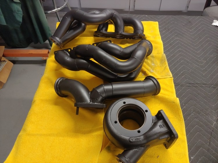 Assorted coated exhaust and turbo parts laid out on a work surface.